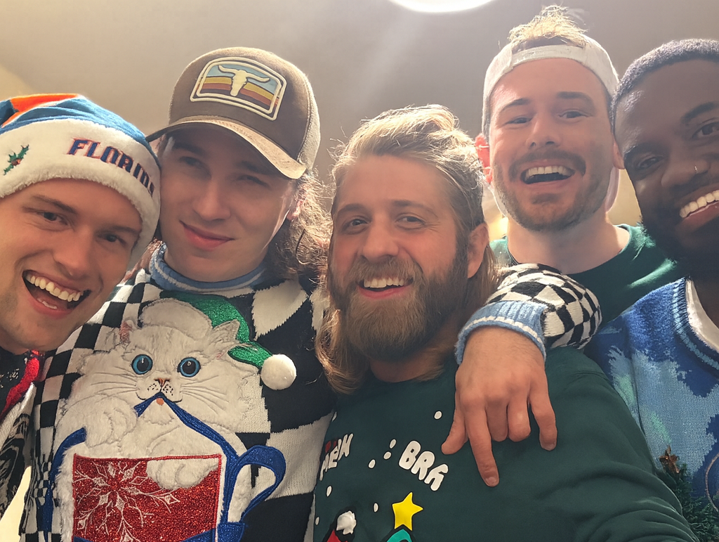 Five friends posing together wearing christmas sweaters in a casual indoor setting.